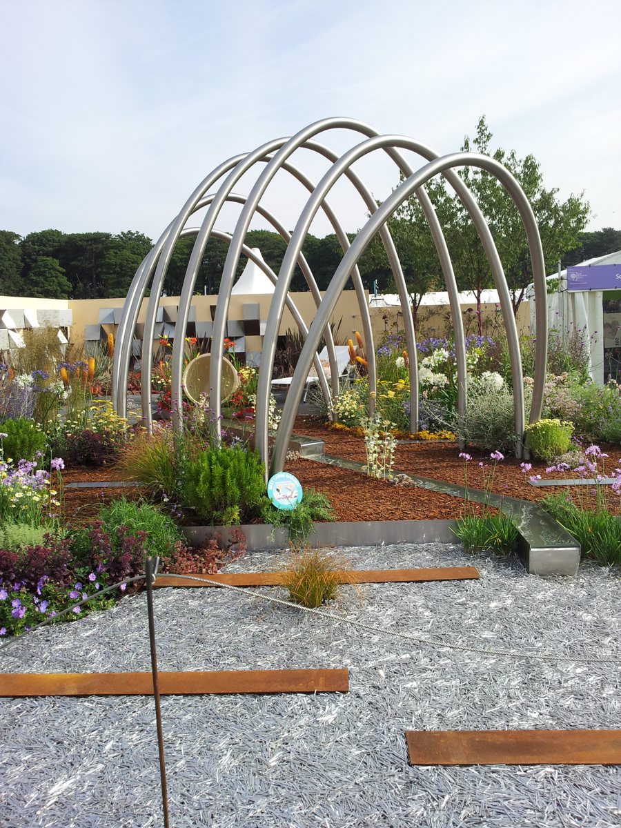 Satin polished stainless steel arched pergola three metres tall in a show garden